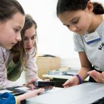 Drei Mädchen arbeiten zusammen an einem Projekt, fokussiert mit technischen Geräten auf einem Tisch.