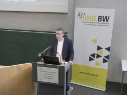 Mann hält Vortrag im KIT am Rednerpult. Im Hintergrund ein Banner des Hochschulnetzwerks Digitalisierung (HND BW).
