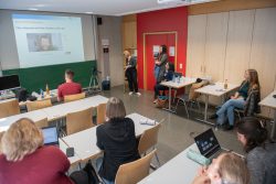 Teilnehmer in einem Seminarraum sehen sich ein Video-Interview auf einer großen Leinwand an.