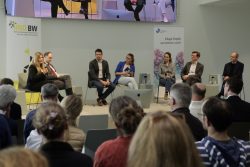 Podiumsdiskussion mit sechs Personen vor Publikum mit dem Banner HND BW. Eine Frau spricht in ein Mikrofon.