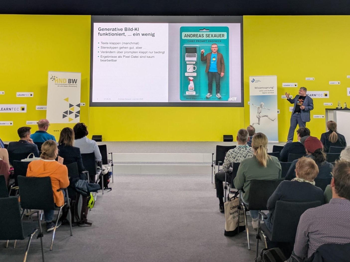 Ein Redner präsentiert über KI bei einer Konferenz. Zuschauer hören aufmerksam zu. Präsentation auf gelbem Hintergrund.