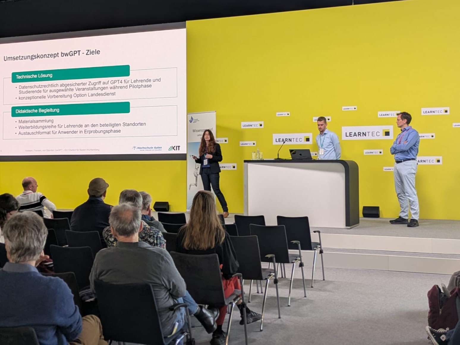 Personen präsentieren auf der LEARNTEC vor Publikum über das Umsetzungs­konzept bwGPT auf einer Bühne mit Bildschirm.