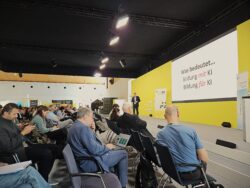 Eine Präsentation über Bildung und KI, gehalten vor Publikum in einem Konferenzraum mit gelber Bühne.