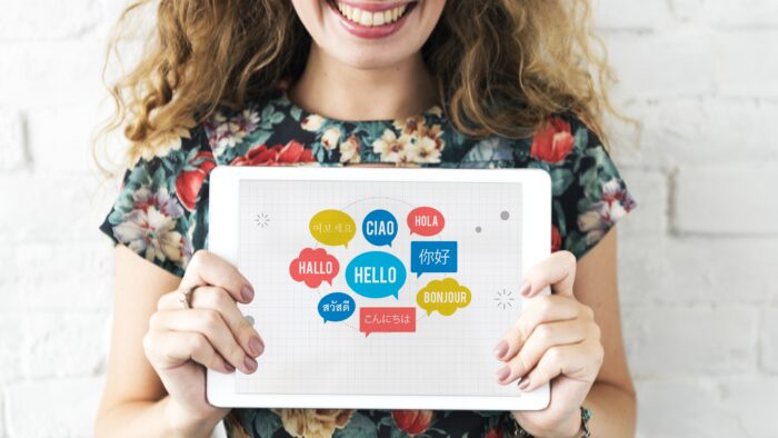 Frau hält ein Tablet mit bunten Sprechblasen, die Hallo in verschiedenen Sprachen anzeigen, lächelnd in der Hand.