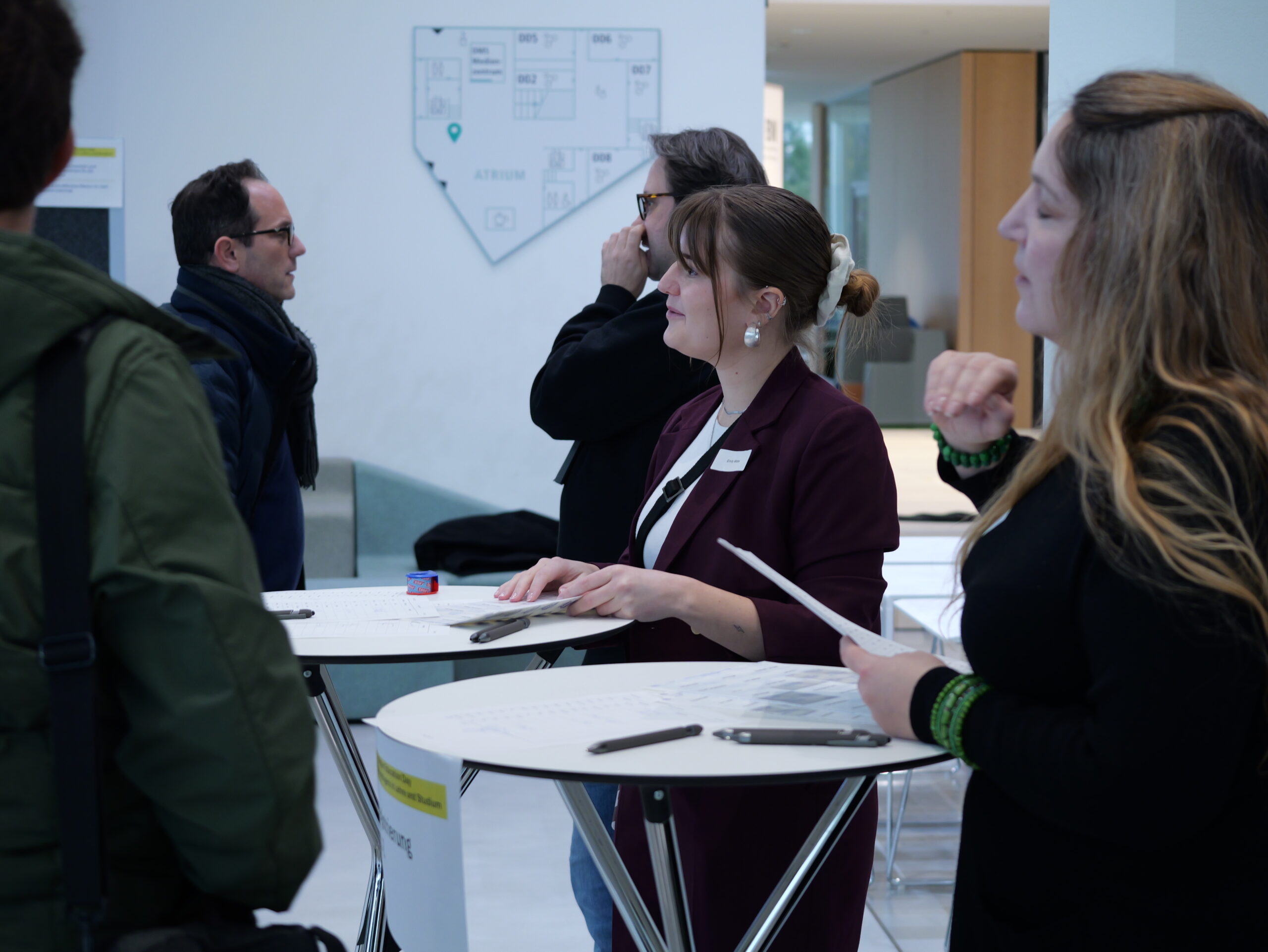 P1001878 Gruppengespräch an Stehtischen in modernem Raum, Teilnehmer diskutieren Dokumente.