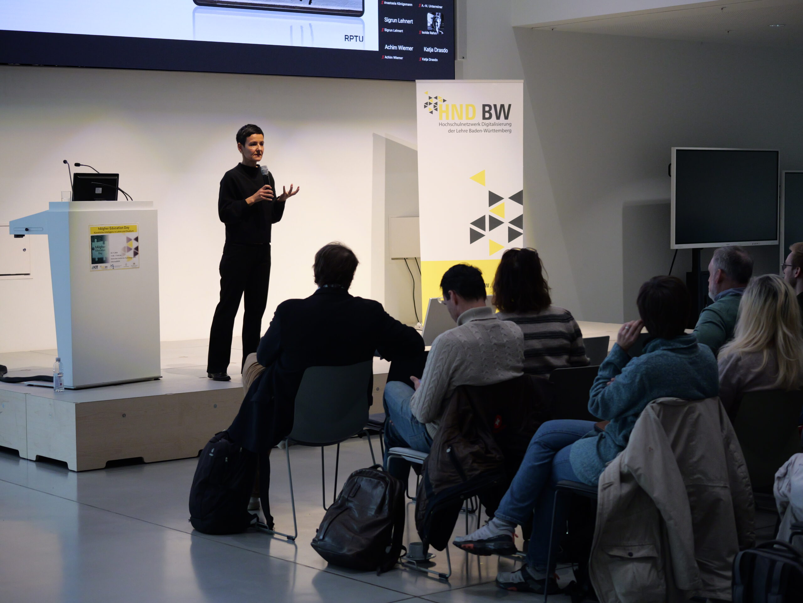 P1002043 - Kopie Eine Person hält einen Vortrag vor sitzendem Publikum in einem modernen Konferenzraum mit Präsentationstechnik.