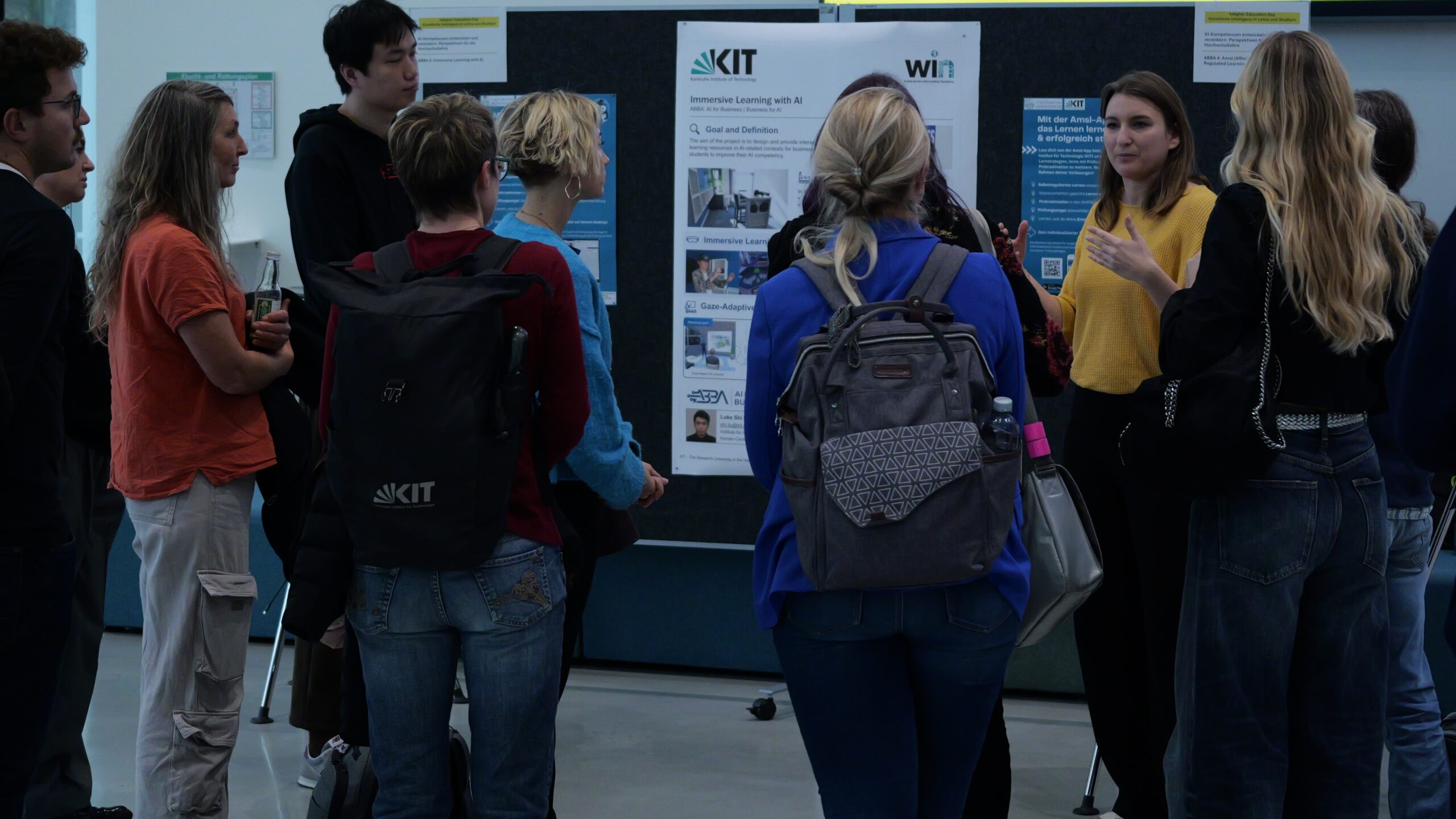 Gruppe von Menschen hört einer Frau bei einer Präsentation vor einem Forschungsposter zu.