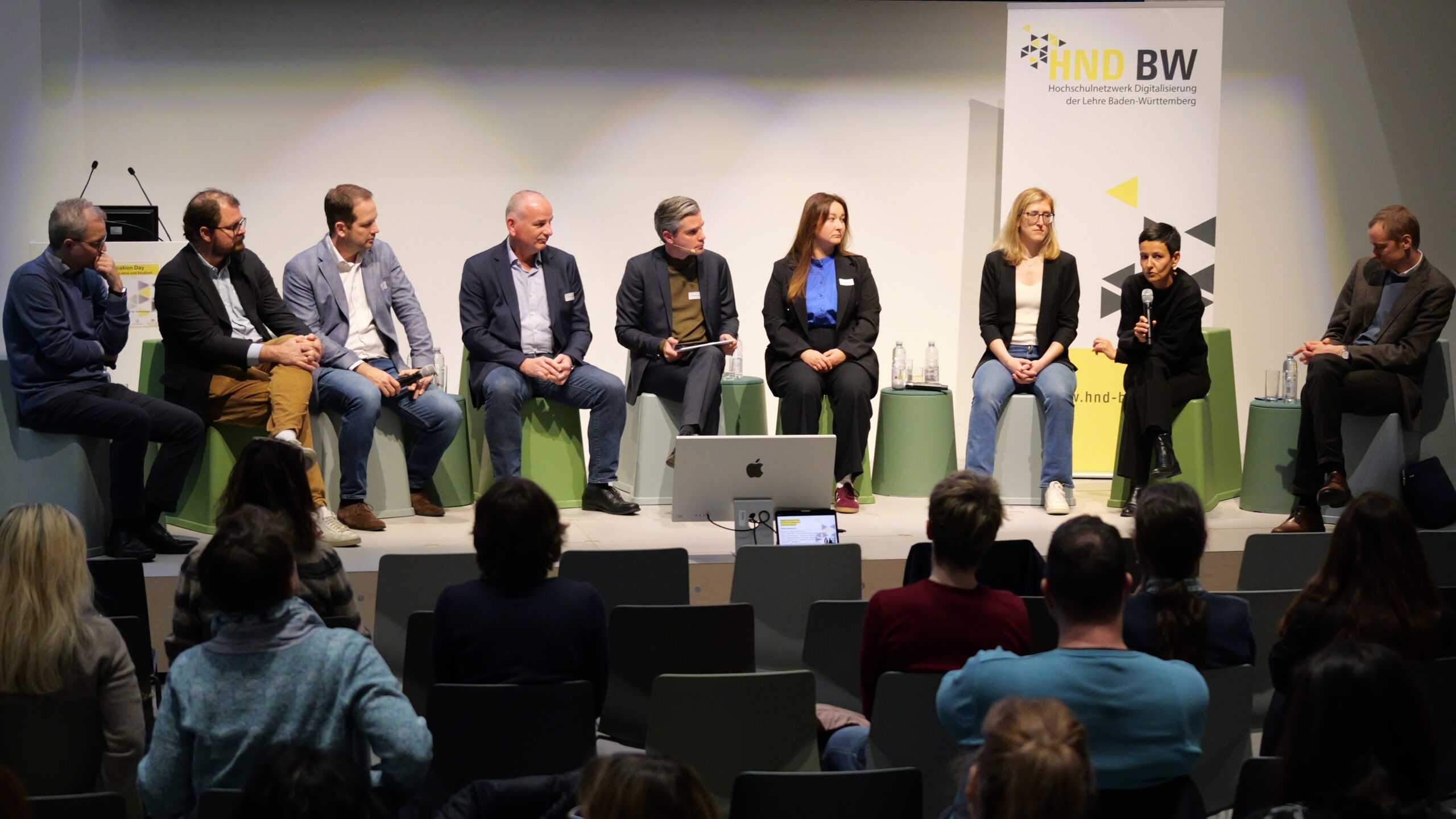 Diskussion mit acht Personen auf einer Bühne vor Publikum, mit HND BW Banner im Hintergrund.