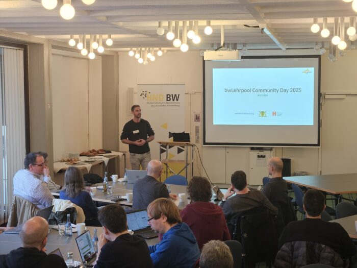 Eine Präsentation beim bwLehrpool Community Day 2025. Der Redner steht vor Publikum, auf der Leinwand ist der Titel zu sehen.